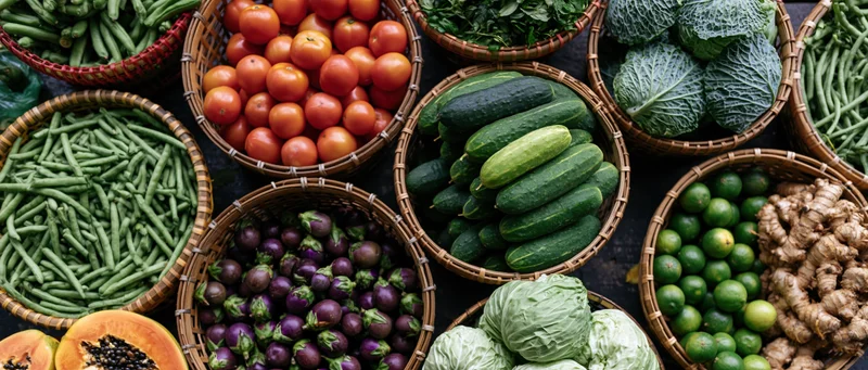 Overhead view of fresh vegetables in woven baskets arranged on a market stall