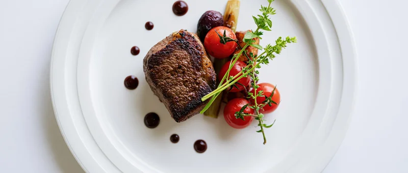 Seared steak with cherry tomatoes and herbs on a white plate, overhead view