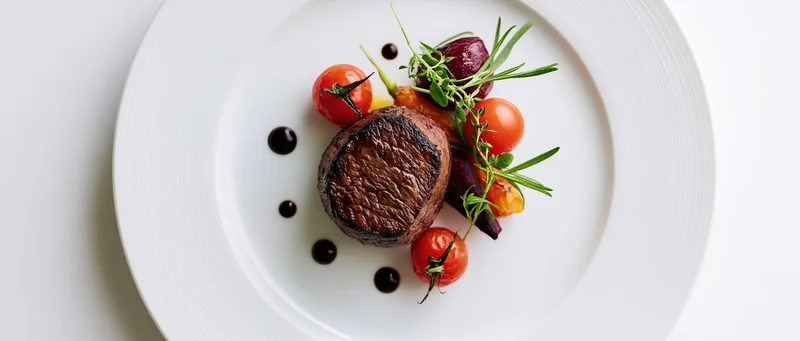 Seared beef steak with cherry tomatoes and rosemary garnish on a white plate, overhead view