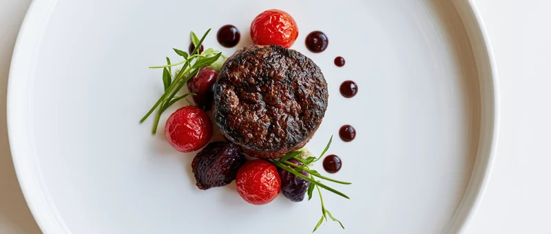 Seared beef steak with cherry tomatoes and herbs on a white plate in fine dining presentation