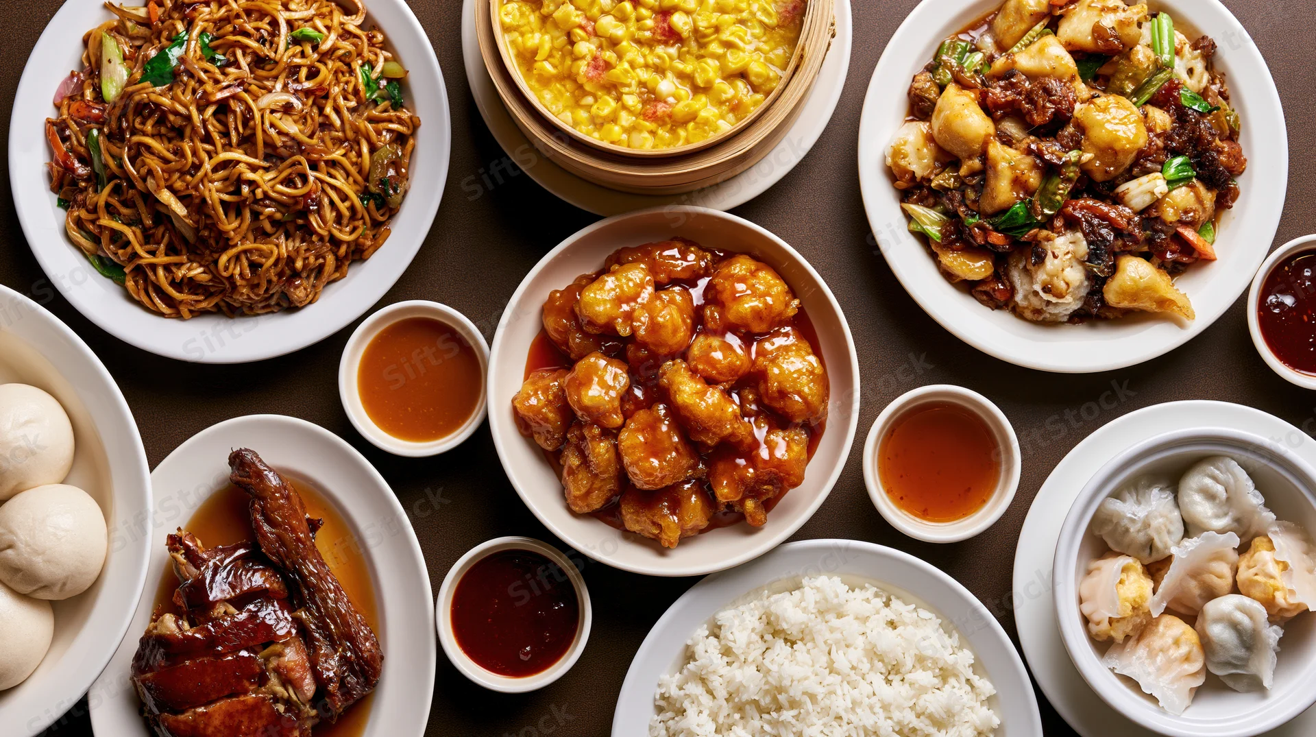 Overhead flat-lay of various Chinese restaurant dishes arranged on a dark surface