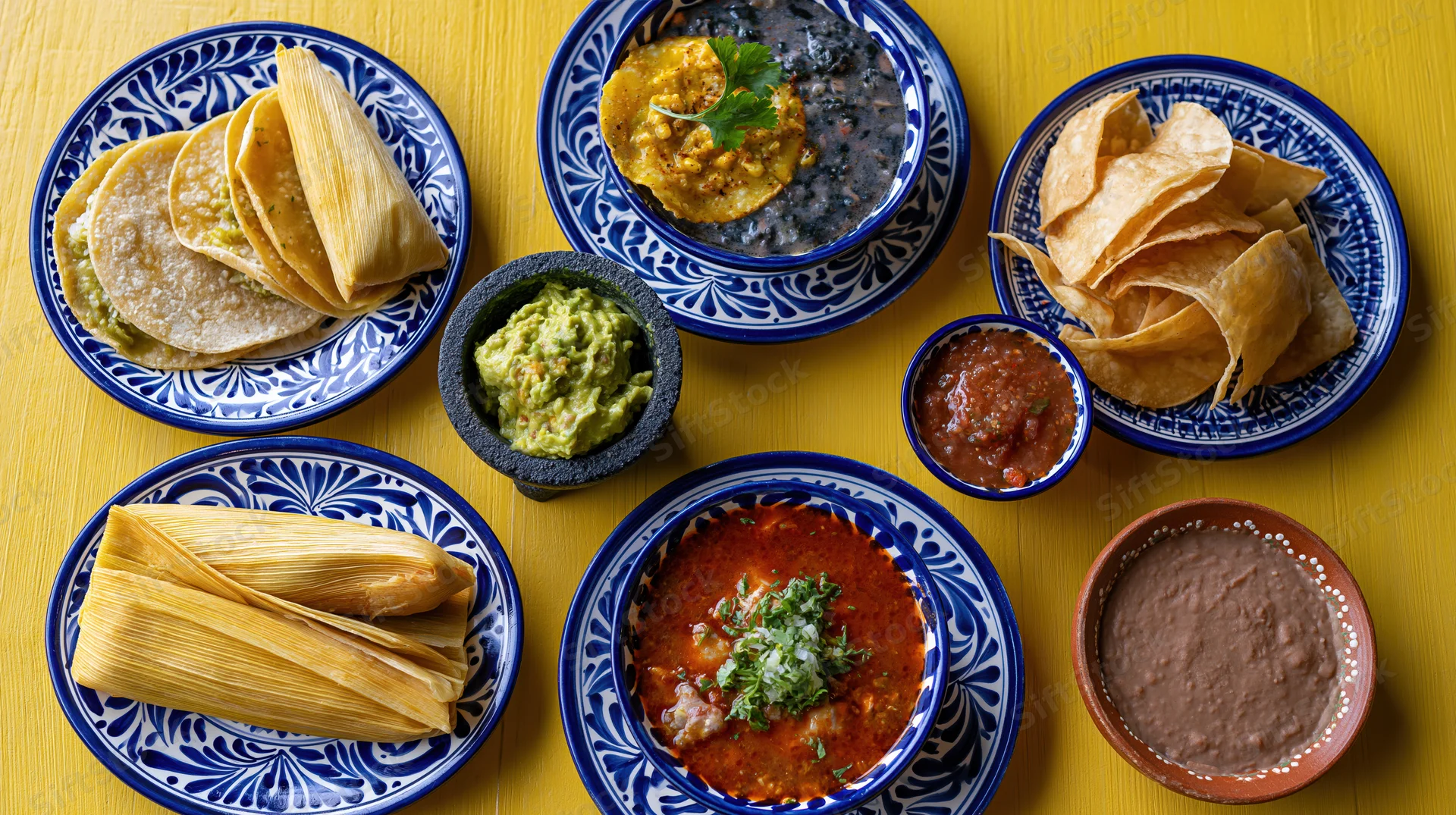Traditional mexican dishes arranged on a yellow table in a flat lay overhead view