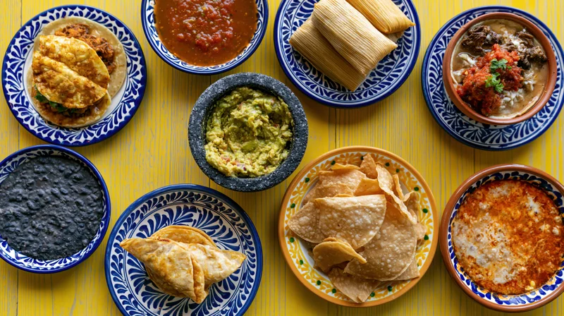Traditional mexican dishes arranged in a flat lay on a yellow table with patterned ceramic plates and bowls