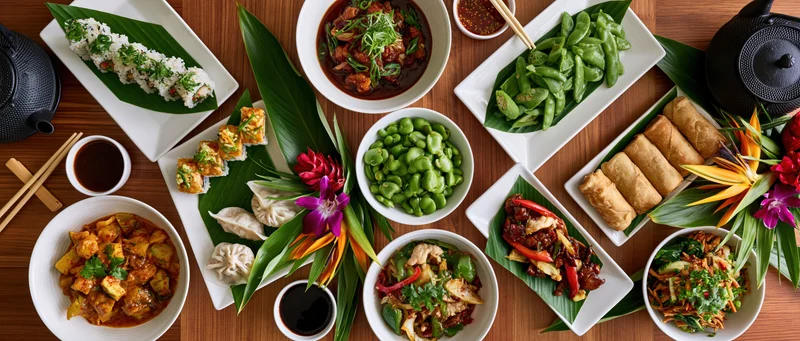 Overhead flat-lay of an elaborate asian restaurant spread with multiple dishes and garnishes on a wooden table