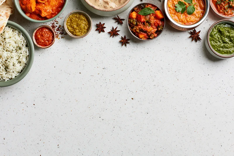 Assorted indian dishes arranged in a flat lay on a white surface with copyspace