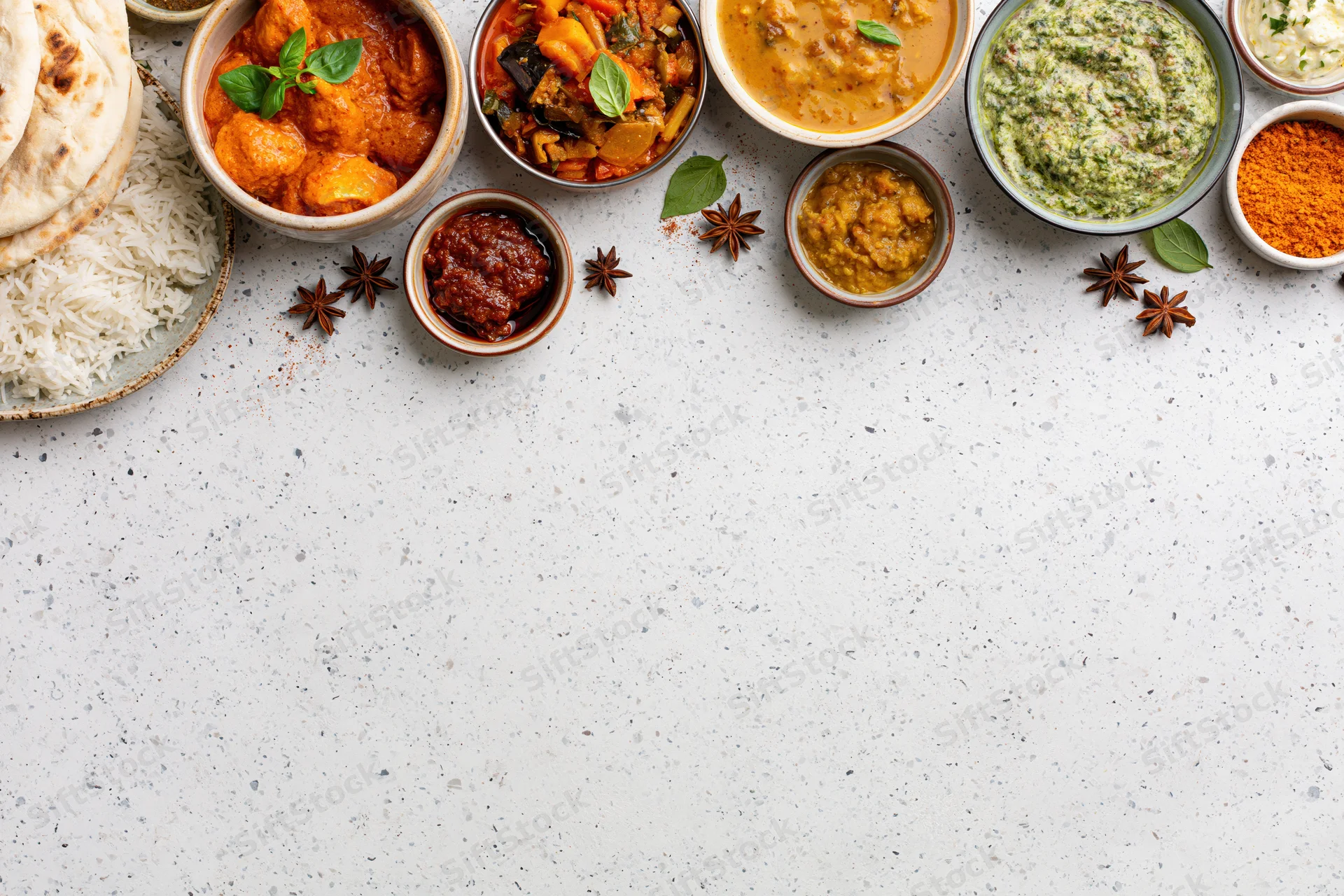 Assorted indian dishes arranged in bowls with rice and naan on a white countertop