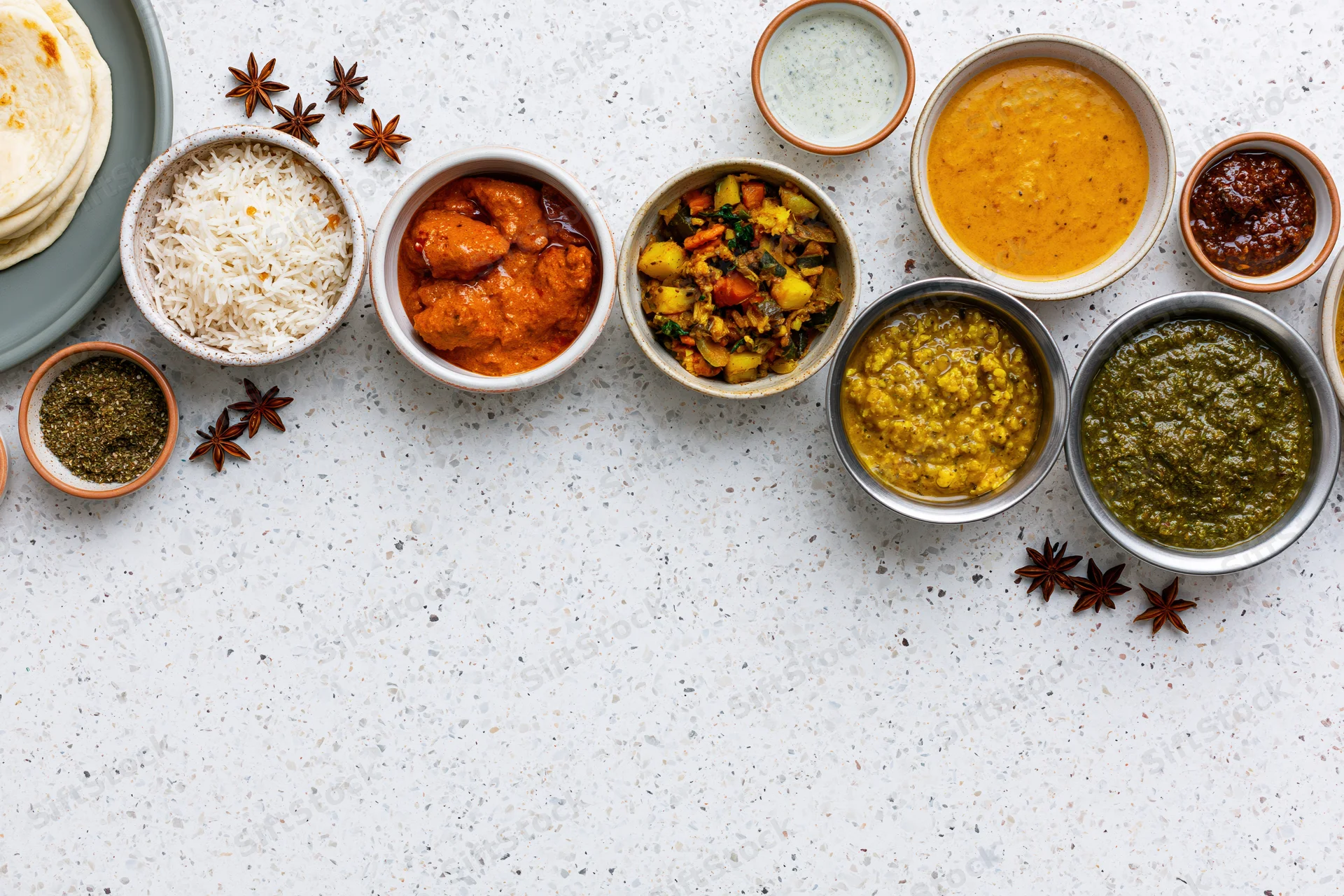 Assorted indian dishes arranged in bowls on a white countertop with copyspace below