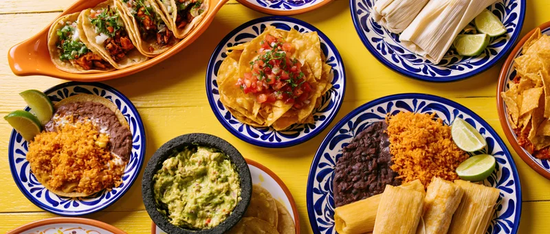 Overhead flat-lay spread of mexican dishes on a bright yellow wooden table