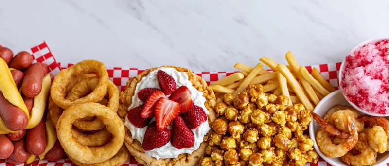 Overhead flat lay of classic american fair foods arranged in a border on a checkered cloth over marble surface