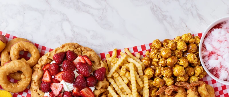 Overhead flat lay of classic american fair foods arranged in a border on a marble countertop with red and white checkered paper