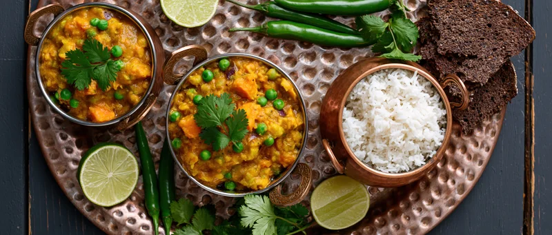 Indian vegetable curry with peas and rice served in copper bowls on a hammered tray with lime and chili garnish