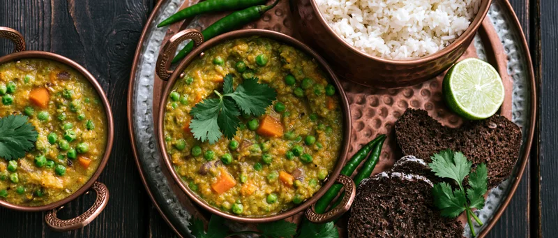 Indian vegetable curry with green peas and lentils served in copper bowls on a tray with rice, lime, and bread