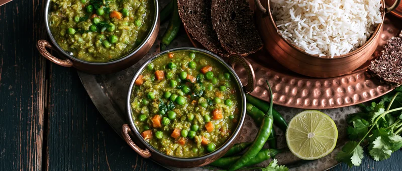 Indian vegetable curry with green peas and rice served on copper bowls and tray with lime and chili garnish