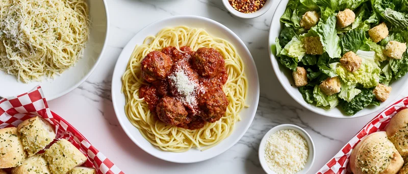 Spaghetti with meatballs and tomato sauce served with garlic bread and salad on a white marble table