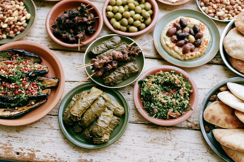 Overhead view of a lebanese mezze spread with hummus, olives, tabbouleh, dolma, eggplant, pita and beans arranged on a worn wooden table