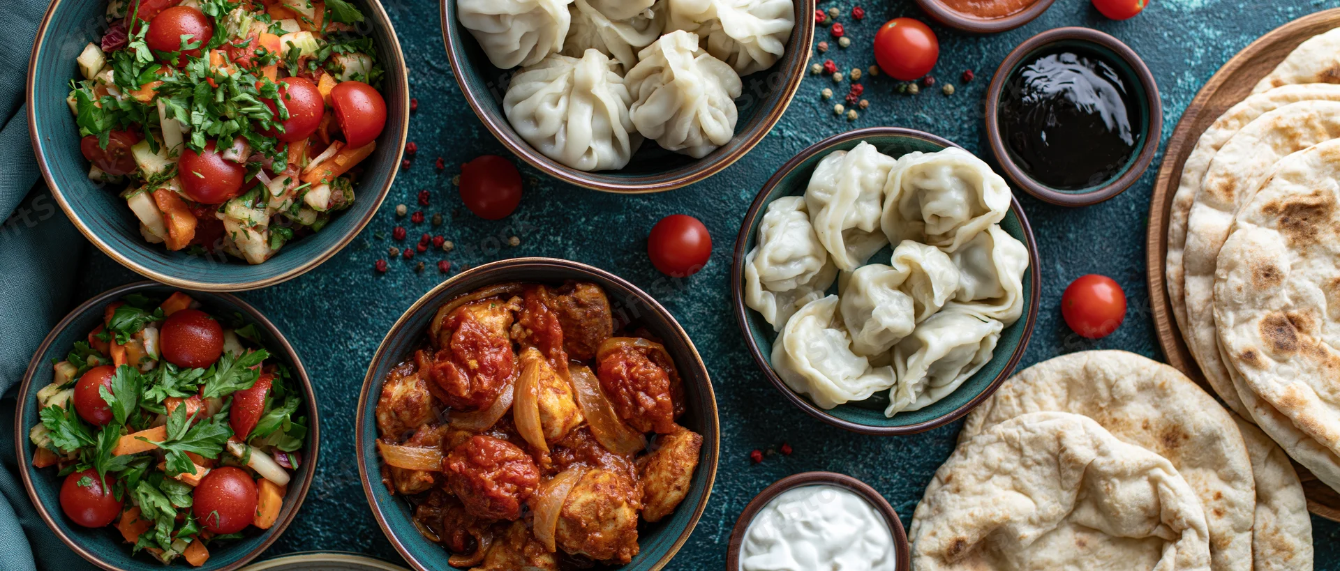 Overhead flat lay of mezze dishes including dumplings, salads, meatballs, flatbread and sauces arranged on a dark blue surface