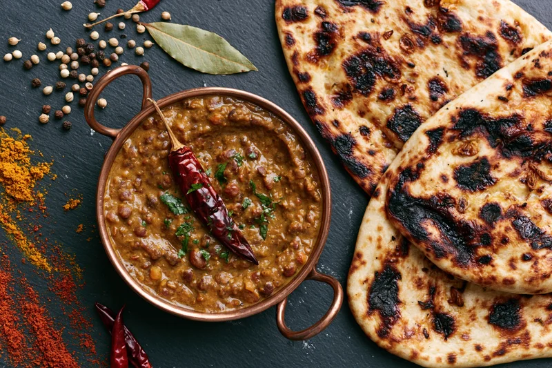 Dal makhani in a copper bowl with naan bread and spices arranged on a dark slate surface