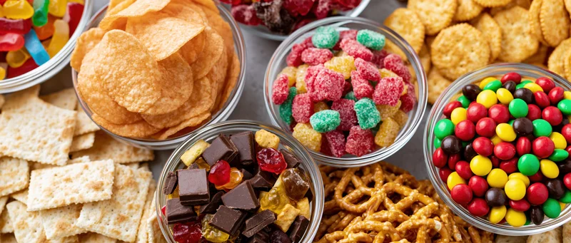 Overhead flat lay of assorted junk food snacks in glass bowls on a gray surface