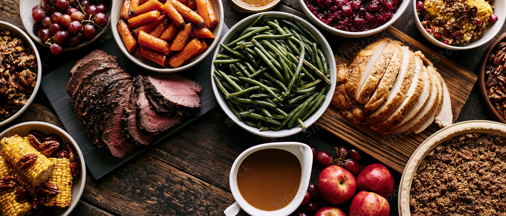 Overhead view of a holiday feast spread with turkey, vegetables, and side dishes on a dark wooden table
