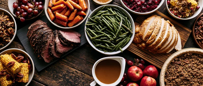 Overhead view of a holiday feast spread with turkey, vegetables, and side dishes on a dark wooden table
