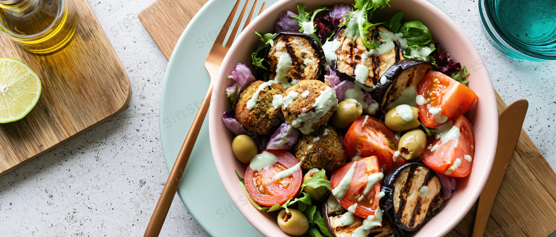 Overhead view of a pink bowl filled with falafel and mixed vegetables on a speckled countertop