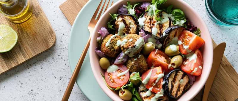 Overhead view of a pink bowl filled with falafel and mixed vegetables on a speckled countertop