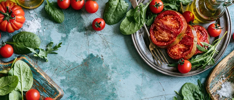 Overhead flat lay of a rustic tomato salad with spinach and arugula on a weathered blue surface