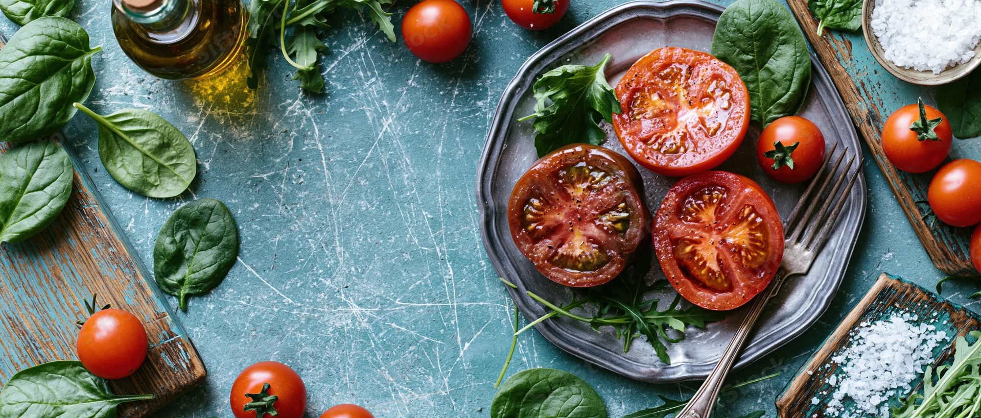 Overhead flat lay of a rustic tomato salad with spinach and arugula on a blue countertop
