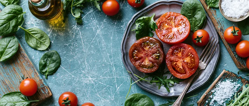 Overhead flat lay of a rustic tomato salad with spinach and arugula on a blue countertop