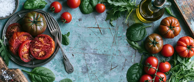 Overhead flat lay of a rustic tomato salad with fresh greens and olive oil on a weathered blue surface