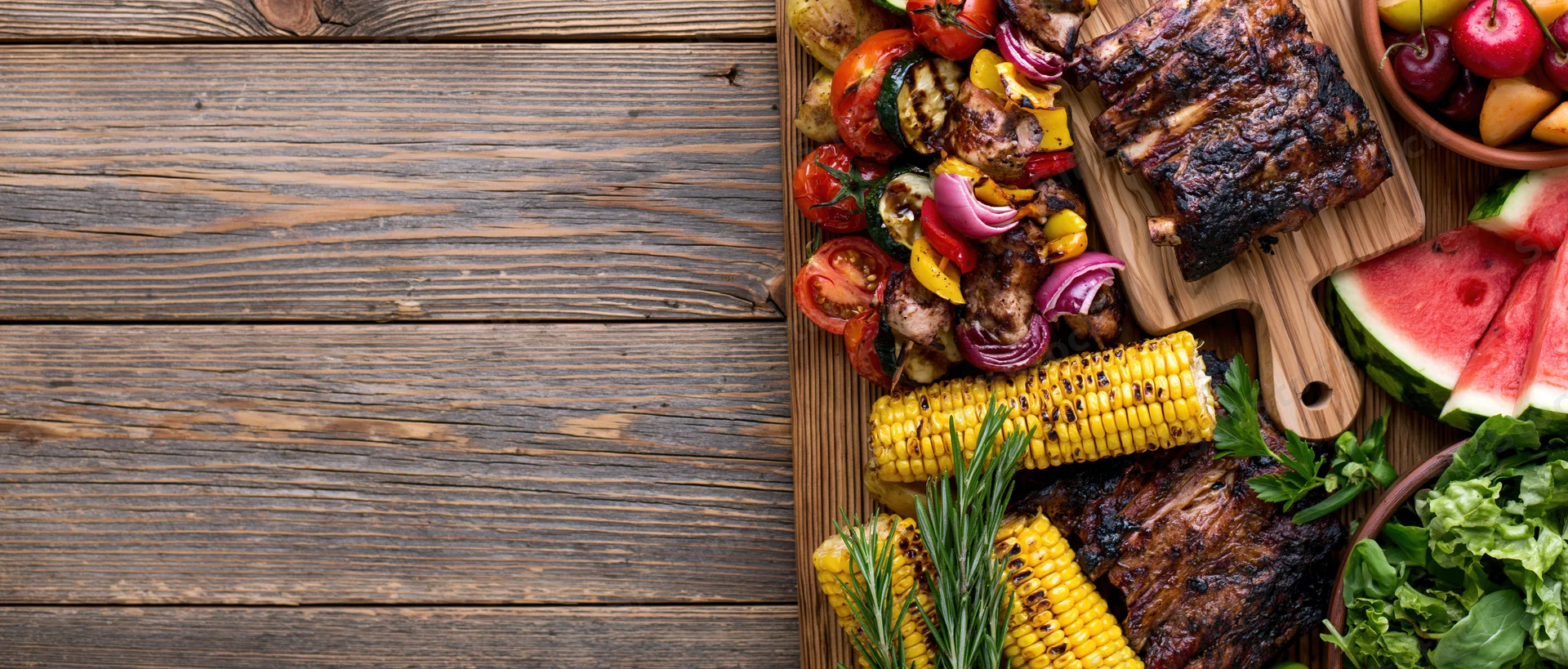 Grilled meats and vegetables arranged on a wooden table with copyspace on the left