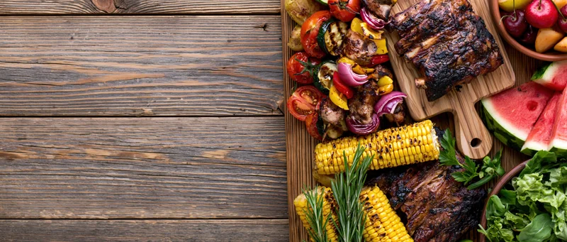 Grilled meats and vegetables arranged on a wooden table with copyspace on the left