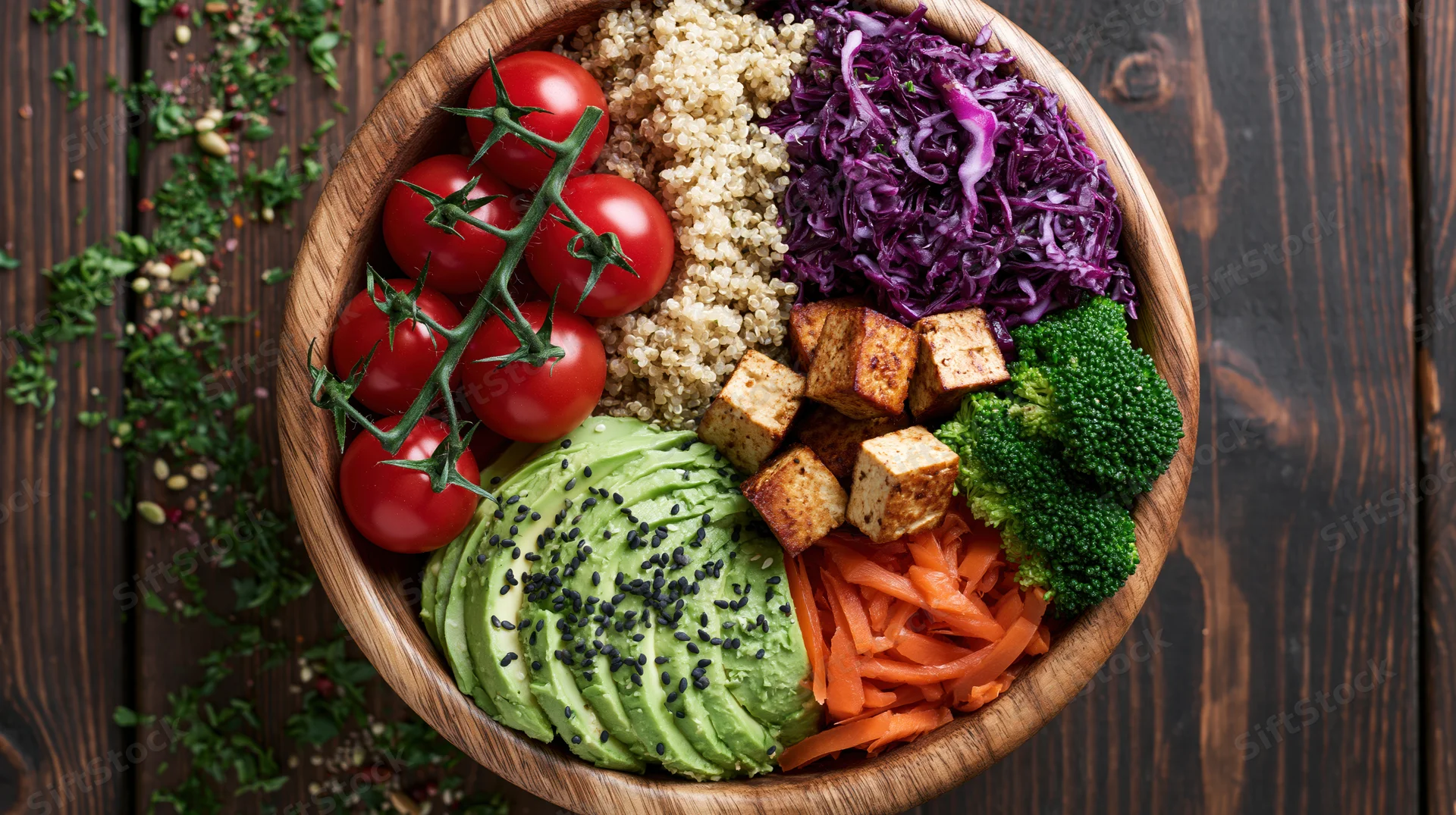 Wooden bowl filled with sliced avocado, quinoa, cherry tomatoes, broccoli, carrots, tofu, and purple cabbage on dark wooden surface