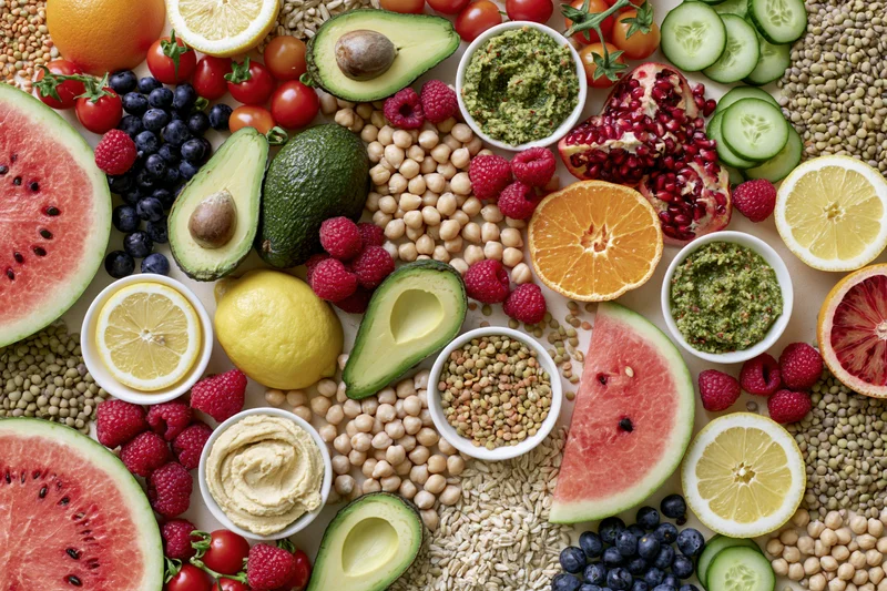 Overhead flat lay of fresh fruits vegetables grains arranged on white surface
