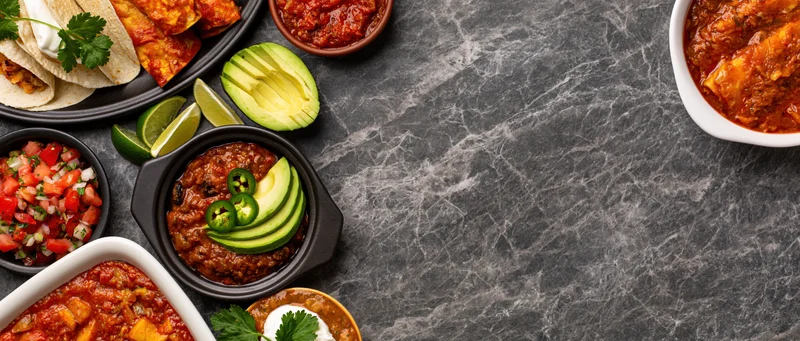 Assorted mexican dishes arranged in flat lay on dark stone surface with copyspace