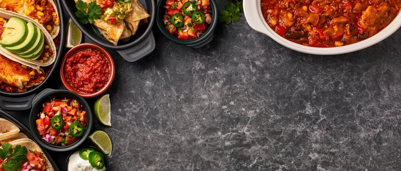 Overhead flat lay of assorted mexican dishes arranged along dark stone countertop with copyspace