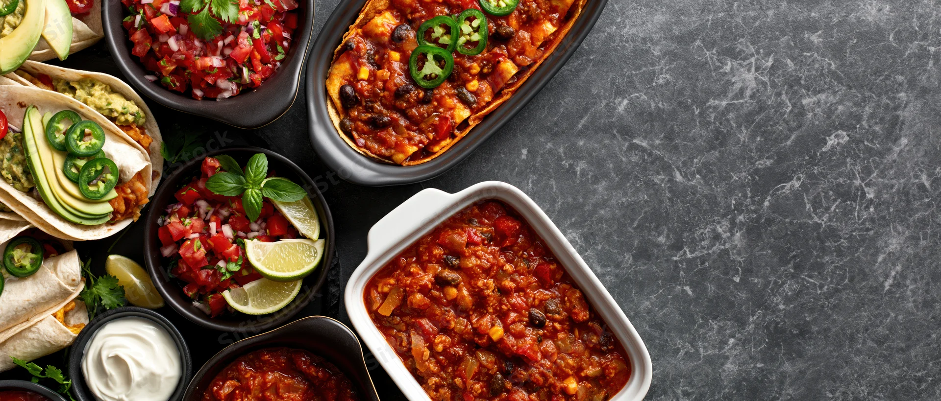 Overhead flat lay of assorted mexican dishes arranged along dark marble countertop with copyspace on right