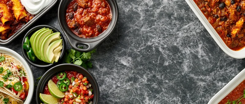 Overhead flat lay of assorted mexican dishes arranged along dark marble countertop with copyspace