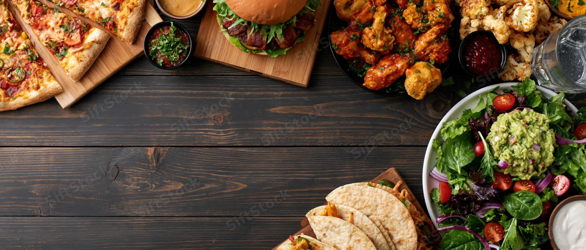 Overhead flat lay of assorted american casual restaurant food on dark wooden table with copyspace