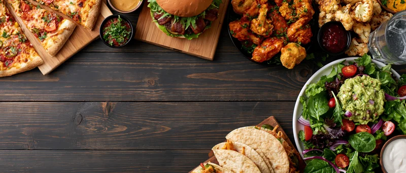 Overhead flat lay of assorted american casual restaurant food on dark wooden table with copyspace