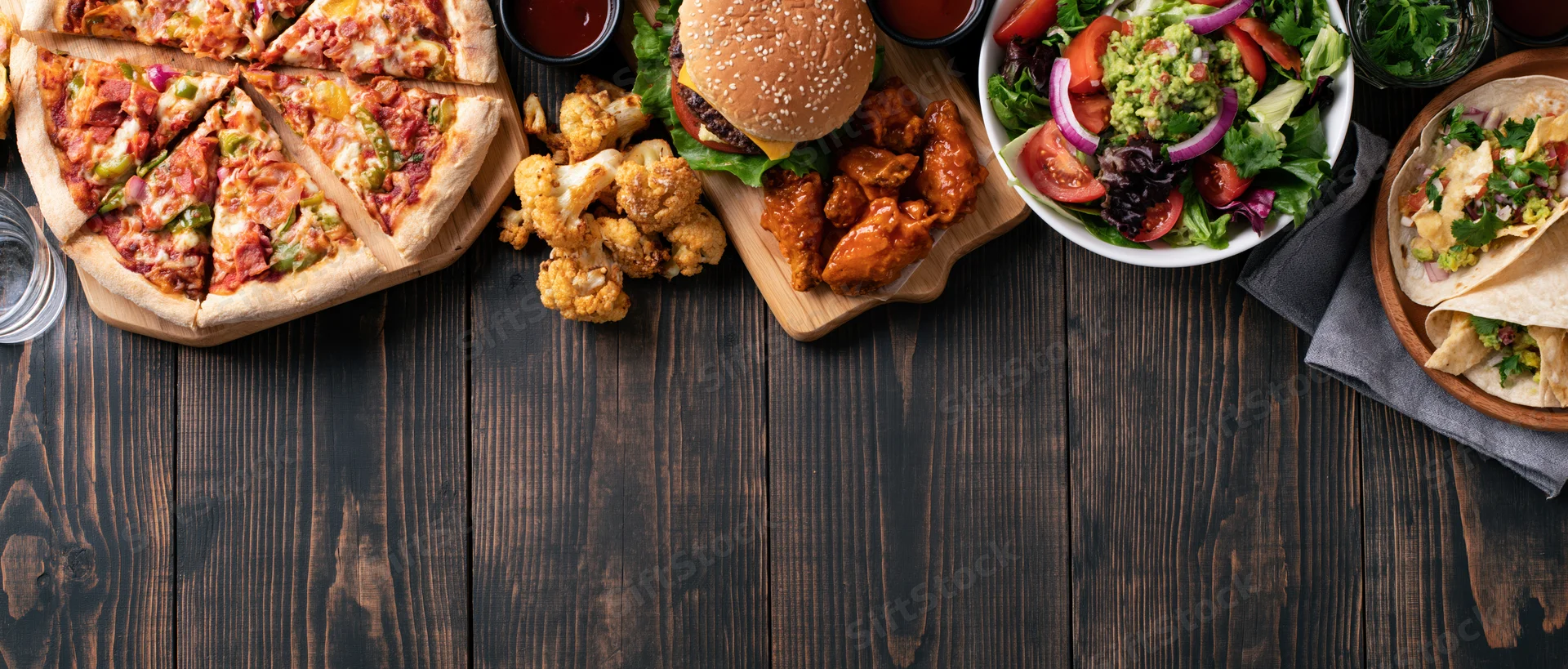 Overhead flat lay of assorted casual american restaurant food on dark wooden table