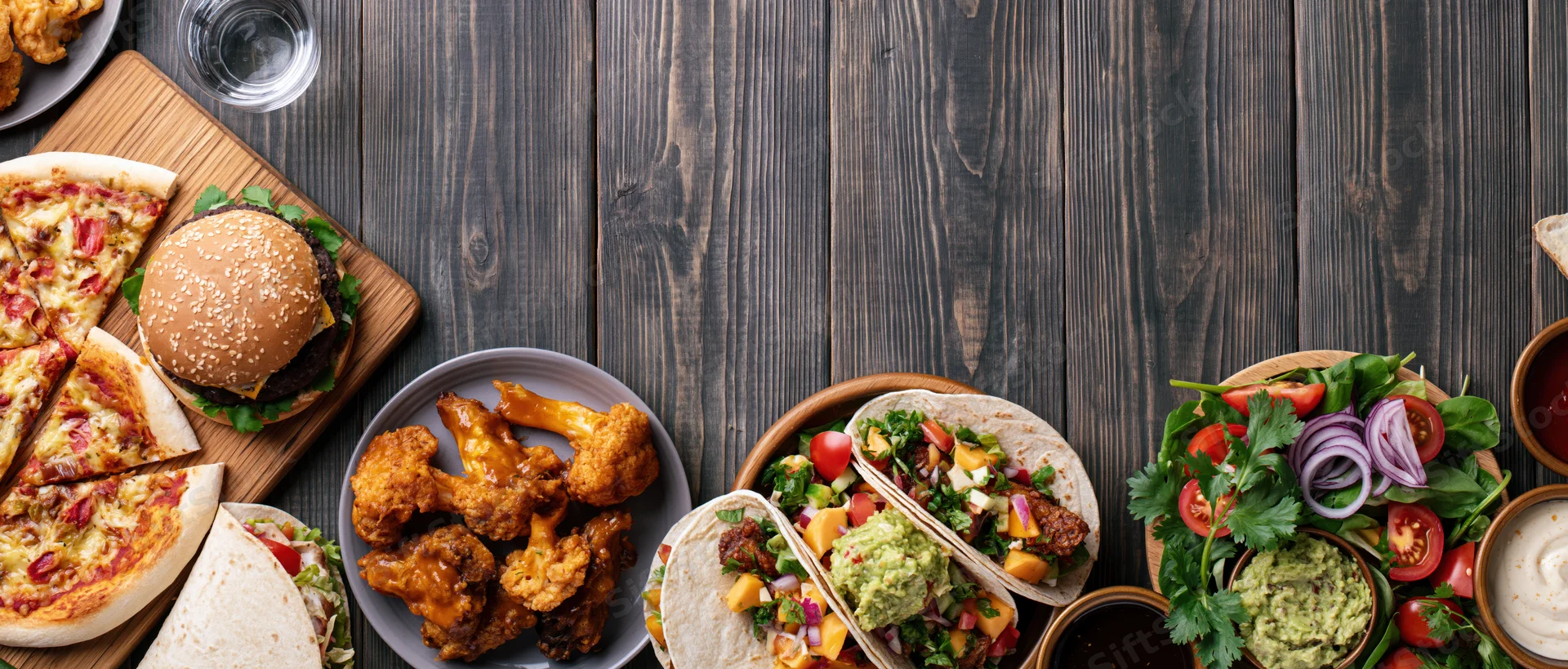 Overhead flat lay of assorted casual american restaurant food on dark wooden table