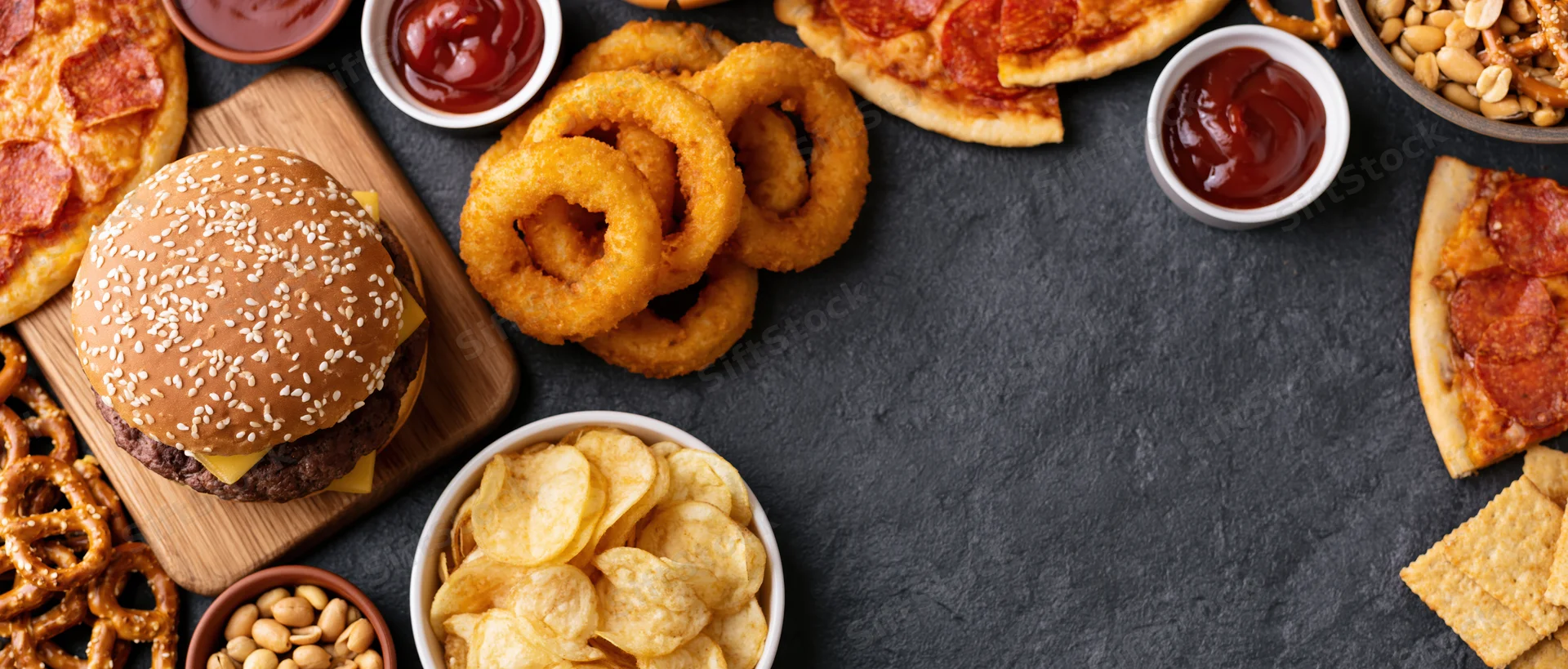 Overhead flat lay of assorted fast food and snacks arranged on dark surface with copyspace