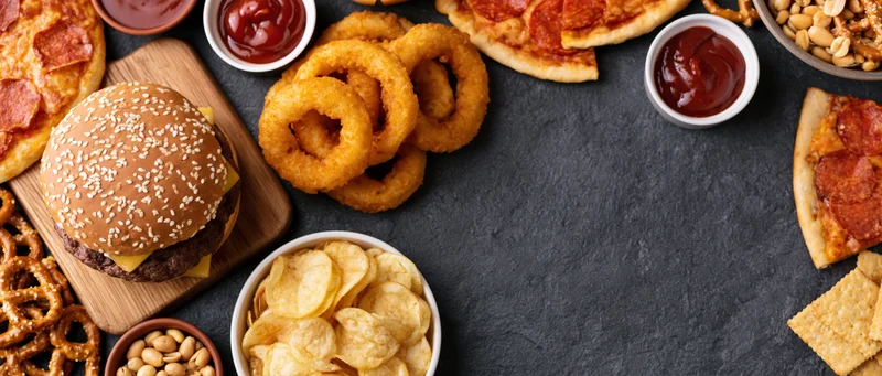 Overhead flat lay of assorted fast food and snacks arranged on dark surface with copyspace
