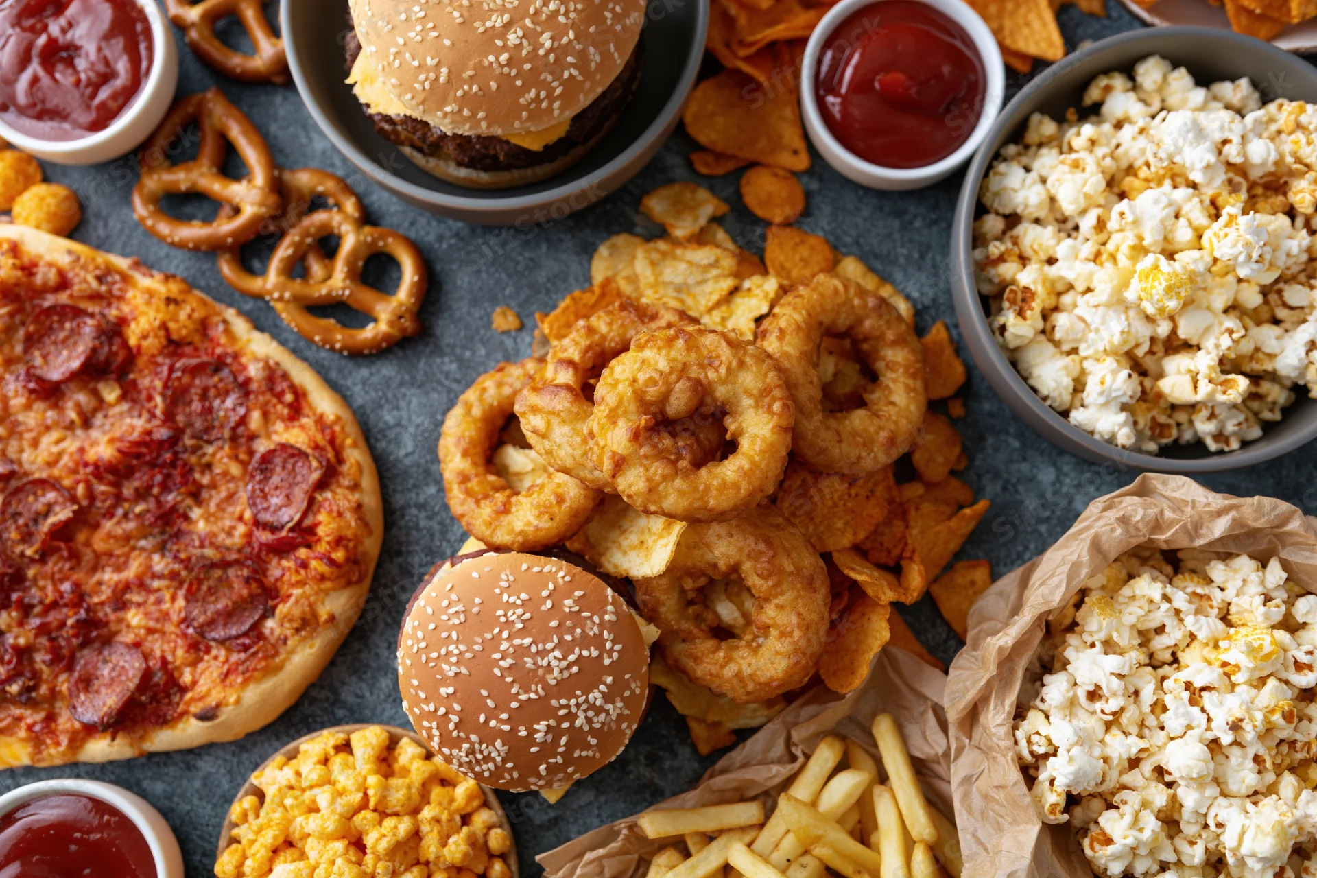 Overhead flat lay of assorted fast food and snacks spread across a dark surface