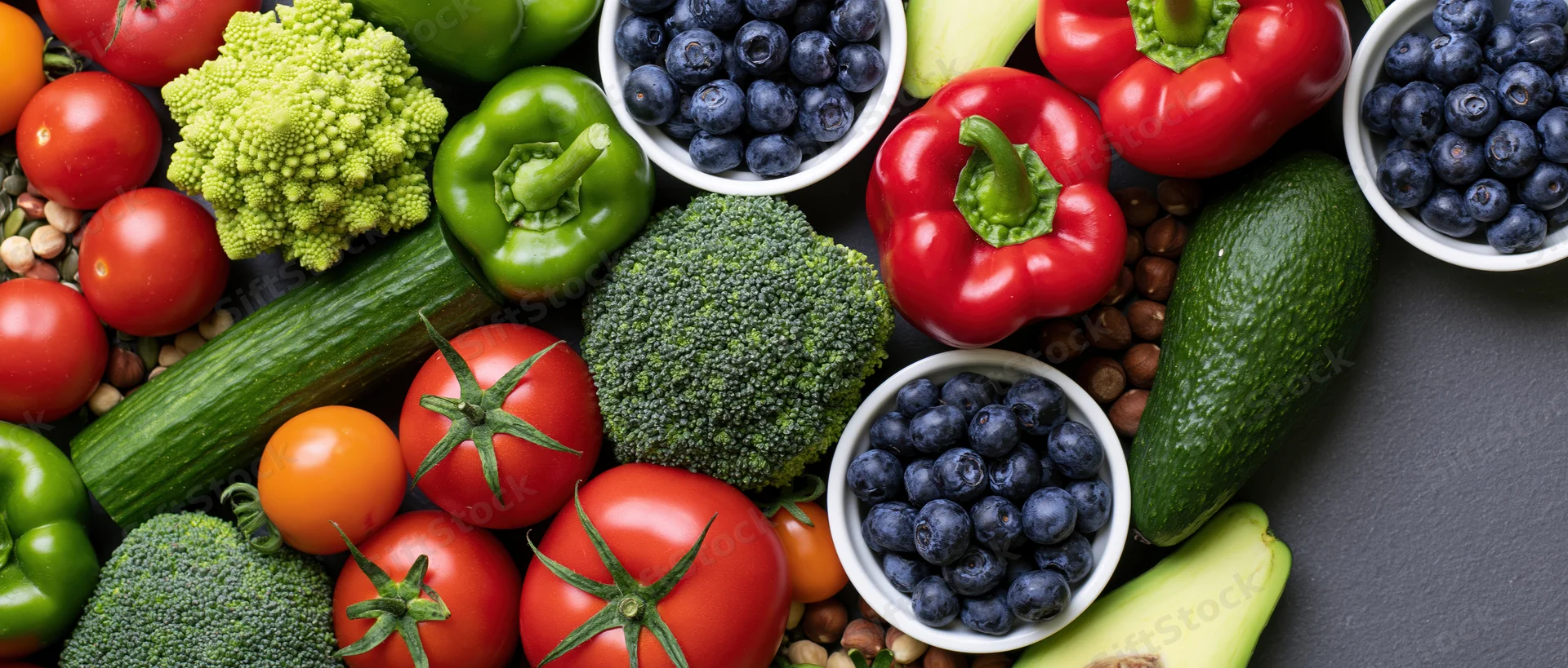 Overhead flat lay of fresh vegetables fruits and nuts arranged on dark surface