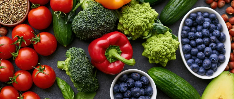 Overhead flat lay of fresh vegetables fruits and nuts on dark stone surface