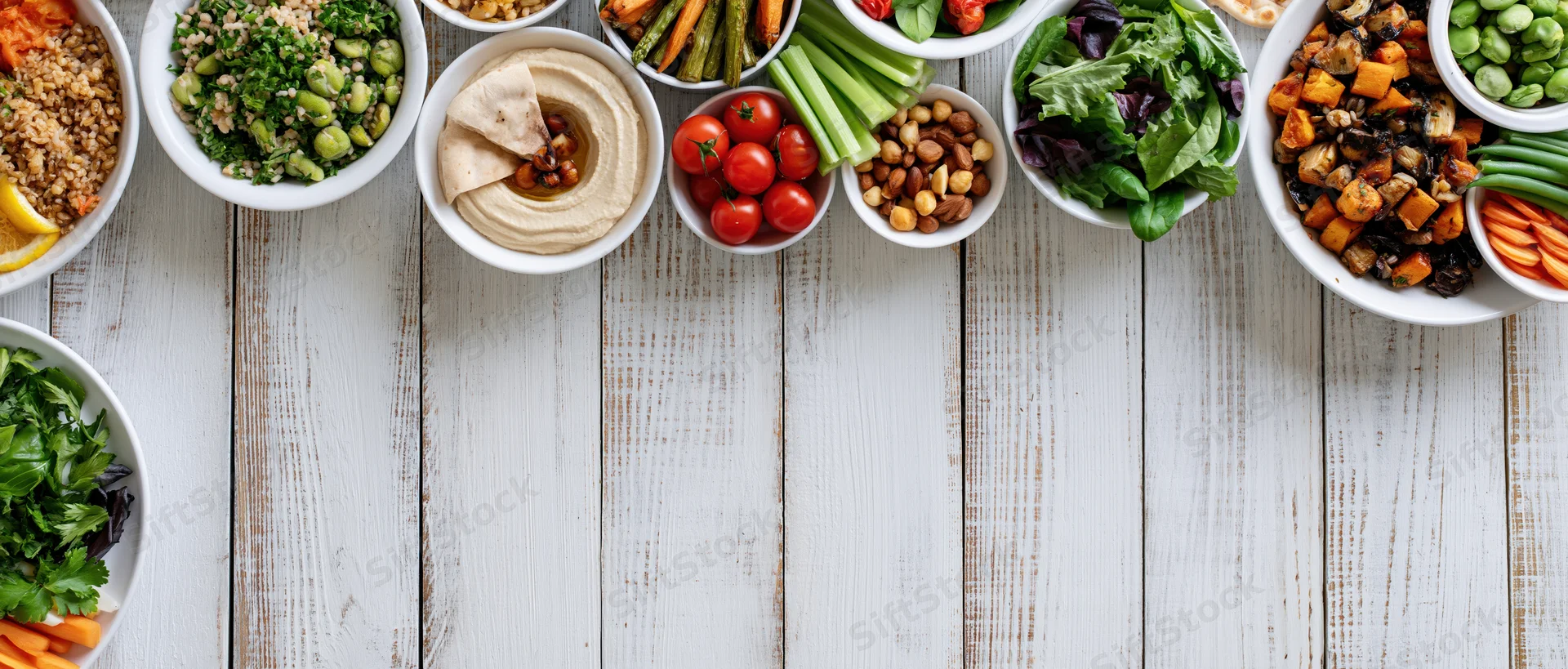 Overhead flat lay of assorted plant-based meals in white bowls on a wooden table