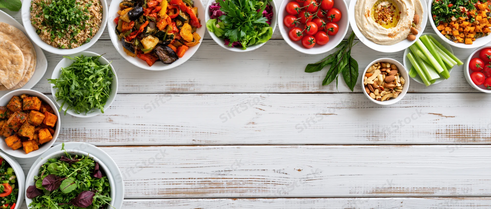 Overhead flat lay of assorted plant-based meals and ingredients arranged on a white wooden table with copyspace
