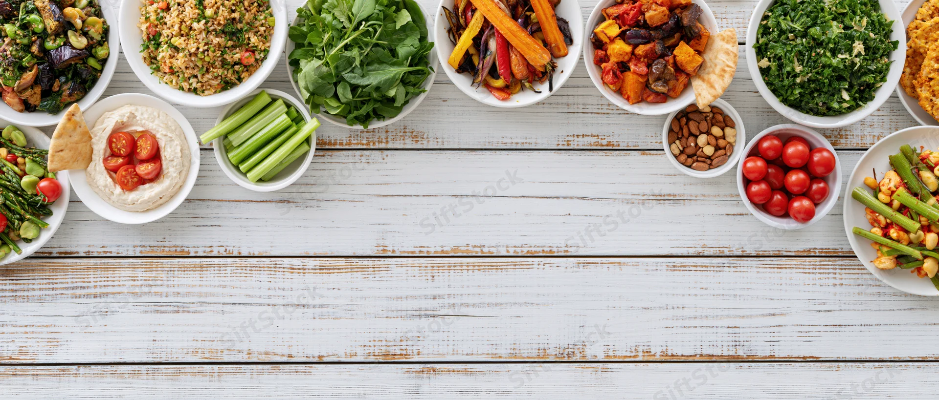 Overhead flat lay of assorted healthy plant-based meals and snacks arranged on a white wooden table with copyspace